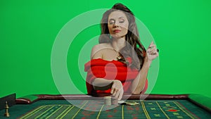 Portrait of female on chroma key green screen close shot. Elegant woman in red dress at the roulette table bets wad of