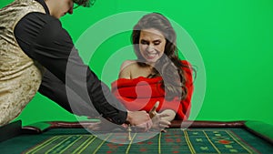 Portrait of female on chroma key green screen close shot. Woman in red dress at the roulette table with croupier wins