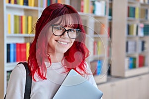 Portrait of female college student in glasses with laptop backpack, looking at camera