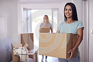 Portrait Of Female Couple Carrying Boxes Through Front Door Of New Home On Moving Day