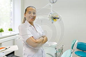 Portrait of female dentist with crossed arms, doctor smiling on dental chair background. Medicine, dentistry and healthcare concep