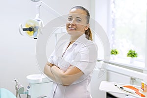 Portrait of female dentist with crossed arms, doctor smiling on dental chair background. Medicine, dentistry and healthcare concep