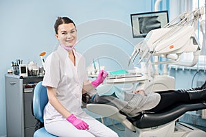 Portrait of female dentist with patient in the dental office. Doctor wearing mask, white uniform and pink gloves