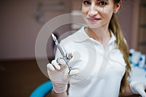 Portrait of a female dentist in white coat posing with syringe filled with anesthesia in a dental cabinet