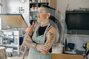 Portrait of female designer standing with crossed hands on background of print machine in workshop