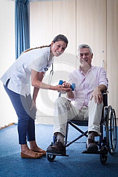 Portrait of female doctor assisting senior man in lifting dumbbell