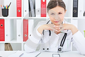 Portrait of a female doctor with hands propped head sitting at the table and looking at the camera.