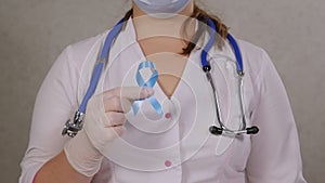 Portrait of a female doctor in a hospital, holding a blue ribbon of awareness.