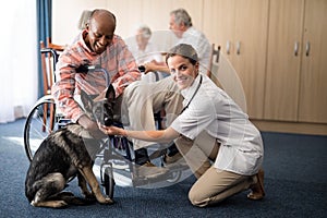 Portrait of female doctor kneeling by disabled senior man stroking puppy