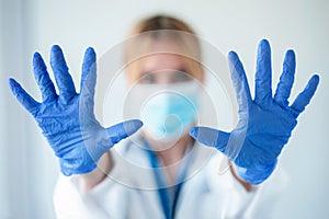 Female doctor with a medical mask showing hands to camera while wearing a blue nitrile gloves over white background photo