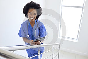 Portrait Of Female Doctor Or Nurse With Digital Tablet Checking Patient Notes On Stairs In Hospital