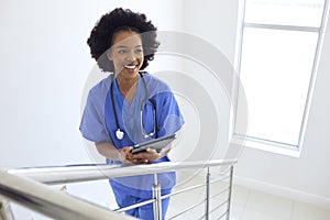 Portrait Of Female Doctor Or Nurse With Digital Tablet Checking Patient Notes On Stairs In Hospital