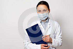 Portrait of a female doctor in a protective mask with a clipboard and a pen in her hands, making a record