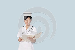 Portrait of a female doctor reading medical report over light blue background