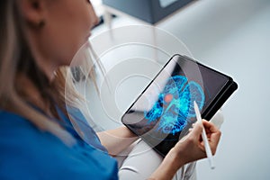 Portrait of female doctor sitting in office, looking at test results CT scans in tablet. Female surgeon in modern