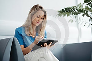 Portrait of female doctor sitting in office, looking at test results CT scans in tablet. Female surgeon in modern