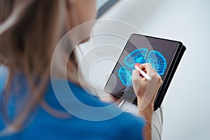 Portrait of female doctor sitting in office, looking at test results CT scans in tablet. Female surgeon in modern