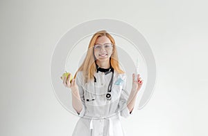 Portrait of a female doctor standing with an apple and a syringe on a light background. The concept of healthy nutrition