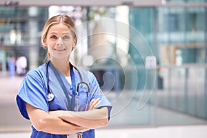 Portrait Of Female Doctor With Stethoscope Wearing Scrubs Standing In Modern Hospital Building photo