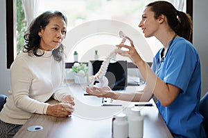 Portrait of a female doctor talking to an elderly patient about herniated disc deterioration from long hours of work.