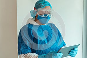 Portrait of a female doctor wearing a medical mask with a digital tablet. Clear wall background, doctor reading writing online.