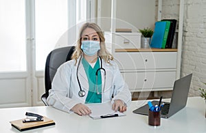 Portrait of female doctor wearing protective surgical mask sitting at clinic office working