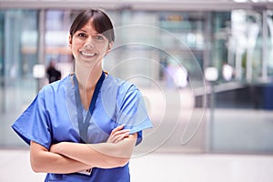 Portrait Of Female Doctor Wearing Scrubs Standing In Modern Hospital Building