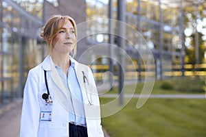 Portrait Of Female Doctor Wearing White Coat Standing Outside Modern Hospital Building