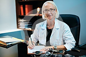 Portrait Of Female Doctor Working In Hospital Office Smiling At Camera