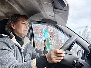 Portrait of female driver in solo journey. Adult mature woman holding steering wheel and bottle of water. Drinking while