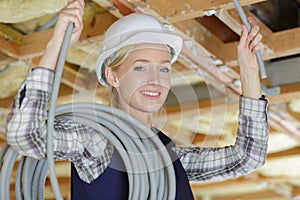 Portrait female electrician feeding electric cable into roofspace