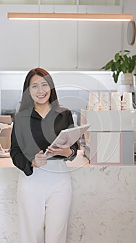 Portrait of female entrepreneur standing behind counter of coffee shop and smiling to camera