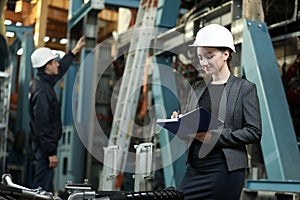 Portrait of a female factory manager in a white hard hat and business suit. Controlling the work process