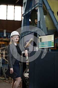 Portrait of a female factory manager in a white hard hat and business suit. Controlling the work process