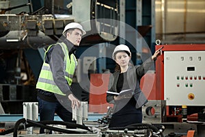 Portrait of a female factory manager in a white hard hat and business suit and factory engineer in work clothes.