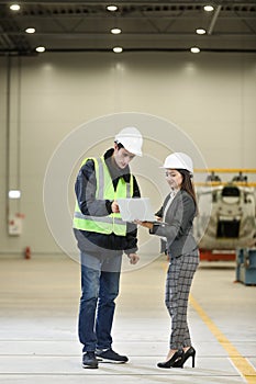 Portrait of a female factory manager in a white hard hat and business suit and factory engineer in work clothes.