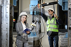 Portrait of a female factory manager in a white hard hat and business suit and factory engineer in work clothes.