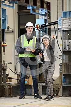 Portrait of a female factory manager in a white hard hat and business suit and factory engineer in work clothes.