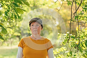 Portrait of female farm worker wearing orange t-shirt and trucker`s hat in walnut tree orchard