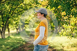 Portrait of female farm worker wearing orange t-shirt and trucker`s hat in walnut tree orchard