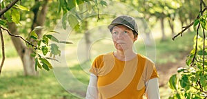 Portrait of female farm worker wearing orange t-shirt and trucker`s hat in walnut tree orchard