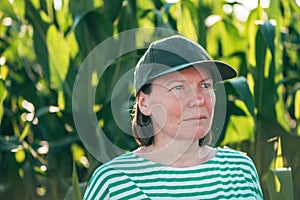 Portrait of female farmer with trucker's hat standing in lush green corn crop field with serious face expression
