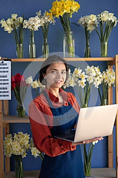 Portrait of a female florist flower shop owner using a laptop in her store. Small business