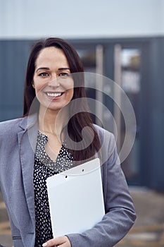 Portrait Of Female Freight Haulage Team Manager Standing By Shipping Container With Clipboard