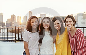 Portrait Of Female Friends Gathered On Rooftop Terrace For Party With City Skyline In Background