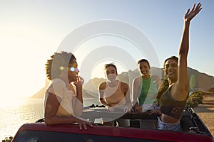 Portrait Of Female Friends Standing Up Through Sun Roof Car And Dancing On Road Trip 