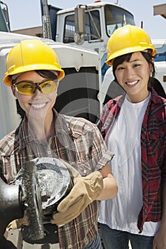 Portrait of female industrial worker buffing a truck engine cylinder with coworker standing besides her