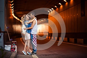 Portrait of female and male skaters embrace passionately, going to kiss, stand against tunnel background, recreat after