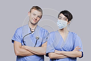 Portrait of female and male surgeons standing with arms crossed over gray background