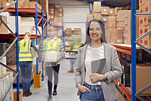 Portrait Of Female Manager With Digital Tablet In Busy Modern Warehouse With Staff In Background